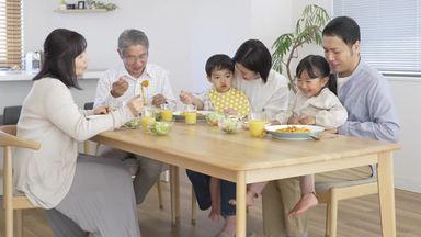 子供が親の膝に座って家族で食事しているところ