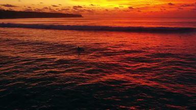 夕日に染まる海とサーフボードに乗る人