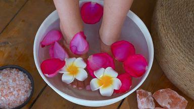 the feet of a woman taking a foot bath in a bowl of flowers