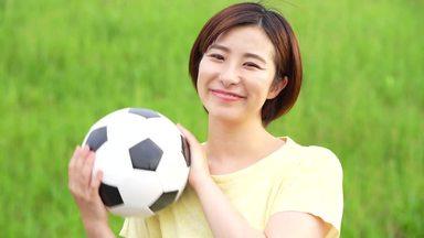 a woman holding a soccer ball with a smile and looking at the camera