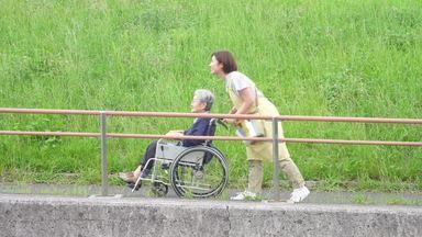a sideways elderly woman climbing a hill in a wheelchair