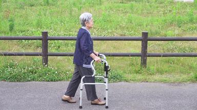 歩行器でゆっくり歩く横向きの高齢女性