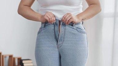 a chubby woman forcing a tight zipper on jeans