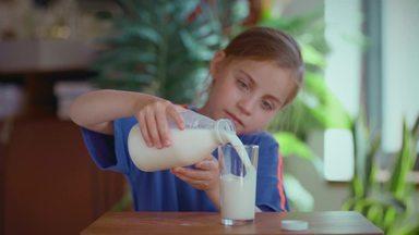 スローでコップに牛乳を注ぐ女の子