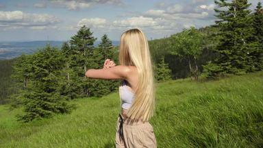 a woman doing a twisting exercise in a mountain meadow
