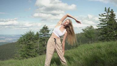 a woman exercising to stretch her side in a mountain meadow