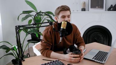 male podcaster holding a paper cup and speaking