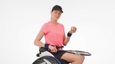 A woman in a wheelchair looking at the camera while throwing and grabbing the ball
